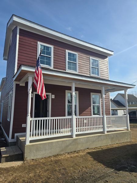 A two-story red house with white trim and an American flag on the porch.
